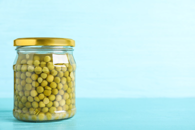 Glass jar of pickled green peas on light blue wooden table. Space for text