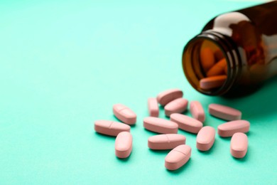 Photo of Vitamin pills and bottle on mint color background, closeup. Space for text