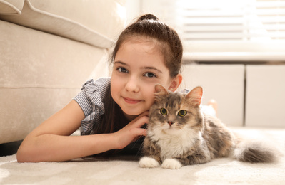 Cute little girl with cat lying on carpet at home. First pet