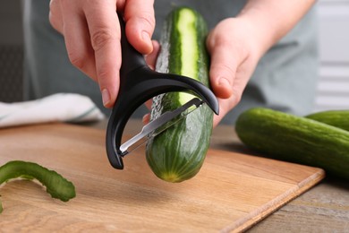 Woman peeling cucumber at wooden table indoors, closeup