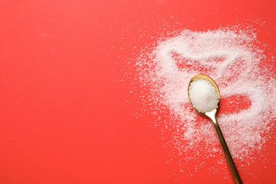 Photo of Granulated sugar and spoon on red background, flat lay. Space for text