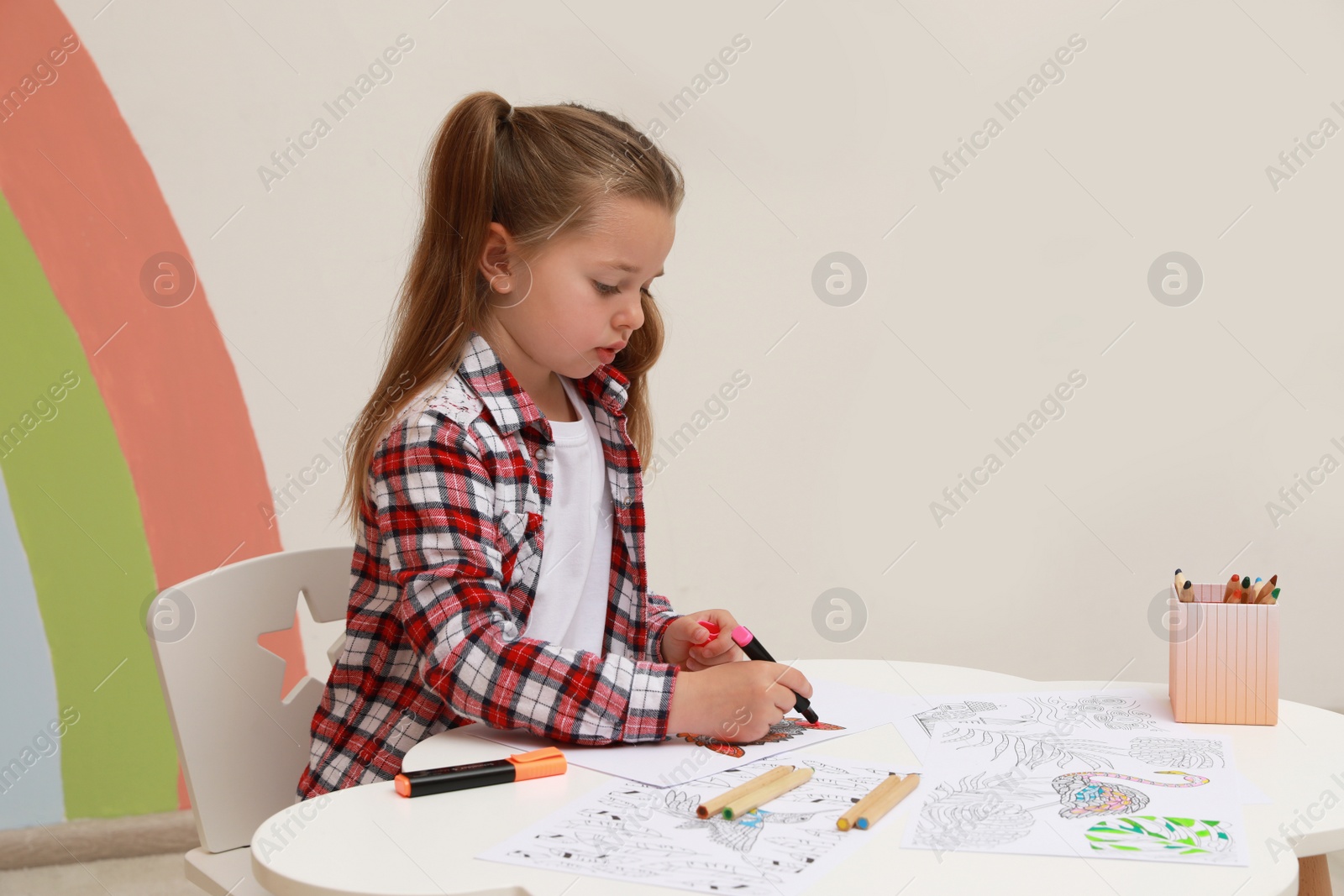 Photo of Little girl coloring antistress page at table indoors