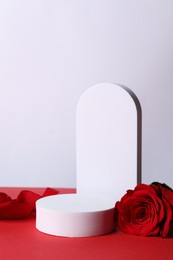 Photo of Stylish presentation for product. Beautiful rose, petals and geometric figures on red table against white background