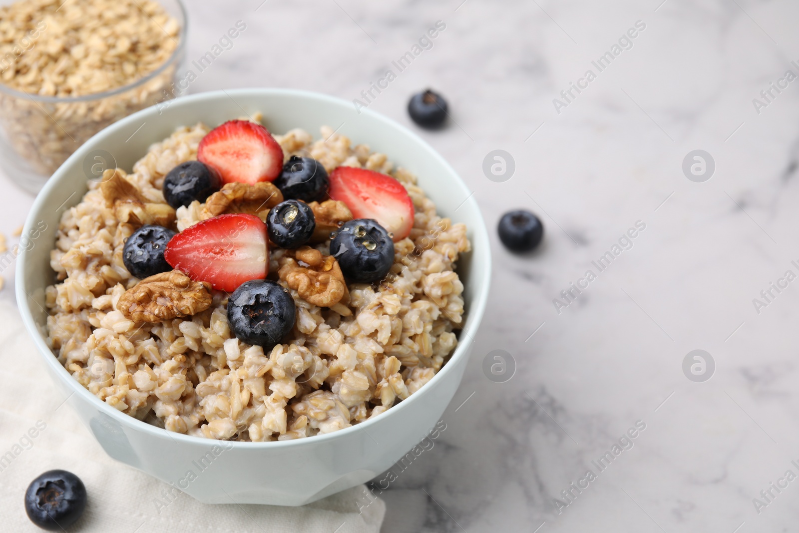 Photo of Tasty oatmeal with strawberries, blueberries and walnuts in bowl on white marble table. Space for text