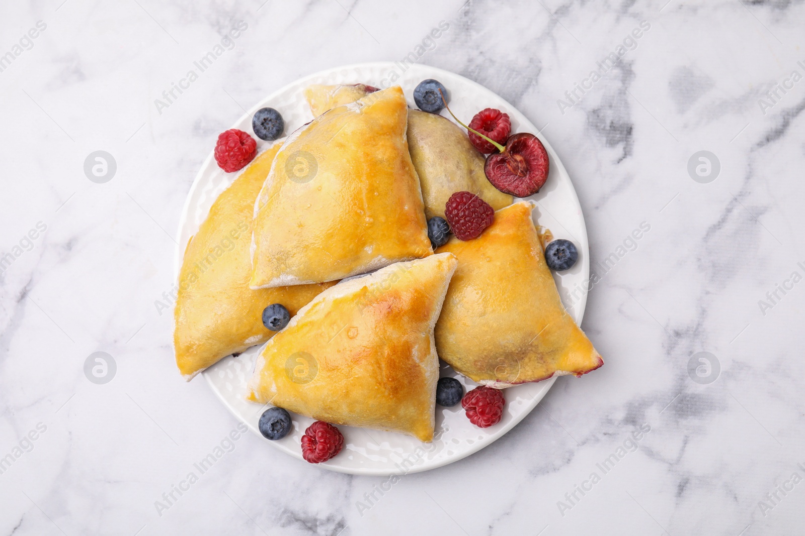 Photo of Delicious samosas with cherry and berries on white marble table, top view