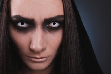 Photo of Mysterious witch with spooky eyes on color background, closeup