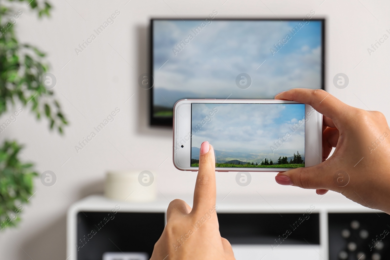 Photo of Woman with smartphone connected to TV set in living room