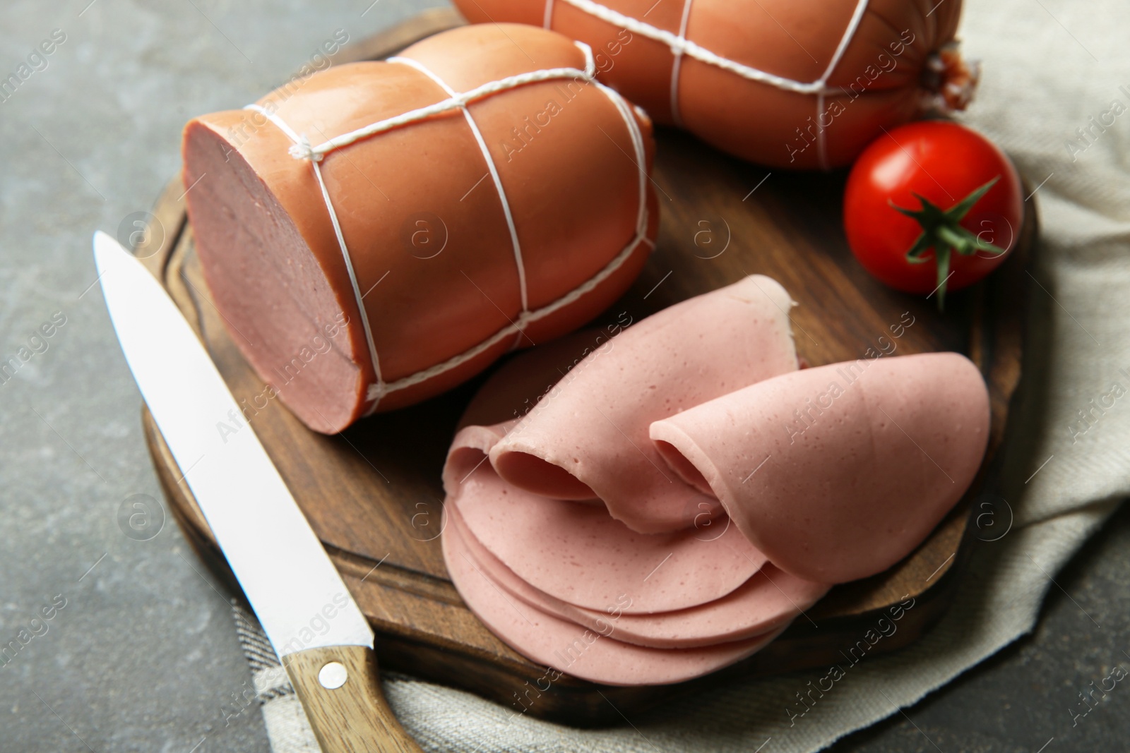 Photo of Board with tasty boiled sausages and tomato on grey textured table, closeup