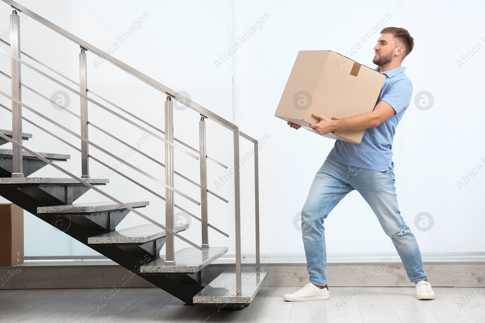 Photo of Young man carrying carton box indoors. Posture concept