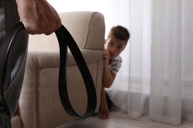 Photo of Man threatens his son at home, focus on belt. Domestic violence concept