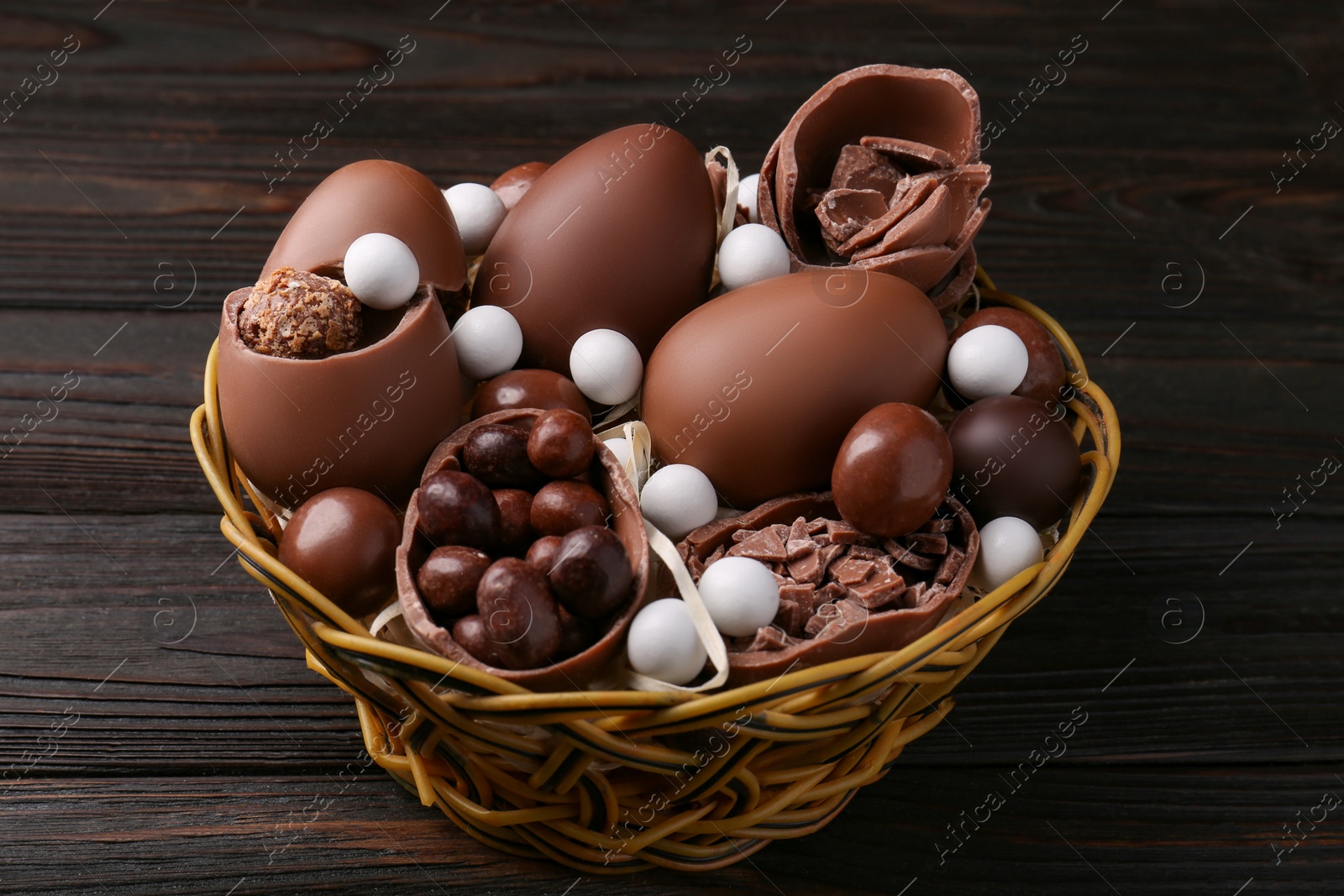 Photo of Tasty chocolate eggs and sweets in wicker basket on wooden table