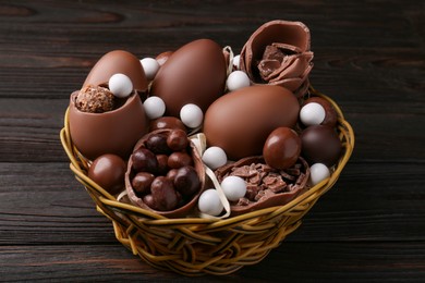 Tasty chocolate eggs and sweets in wicker basket on wooden table