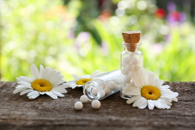 Photo of Bottles of homeopathic remedy and beautiful flowers on wooden table, space for text