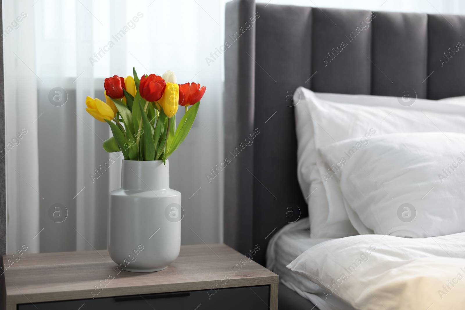 Photo of Beautiful tulips in vase on bedside table indoors