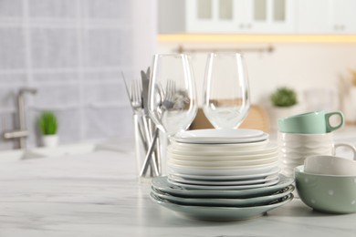 Many different clean dishware and glasses on white marble table in kitchen. Space for text