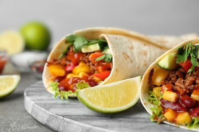 Photo of Board with delicious meat tortilla wraps on table, closeup