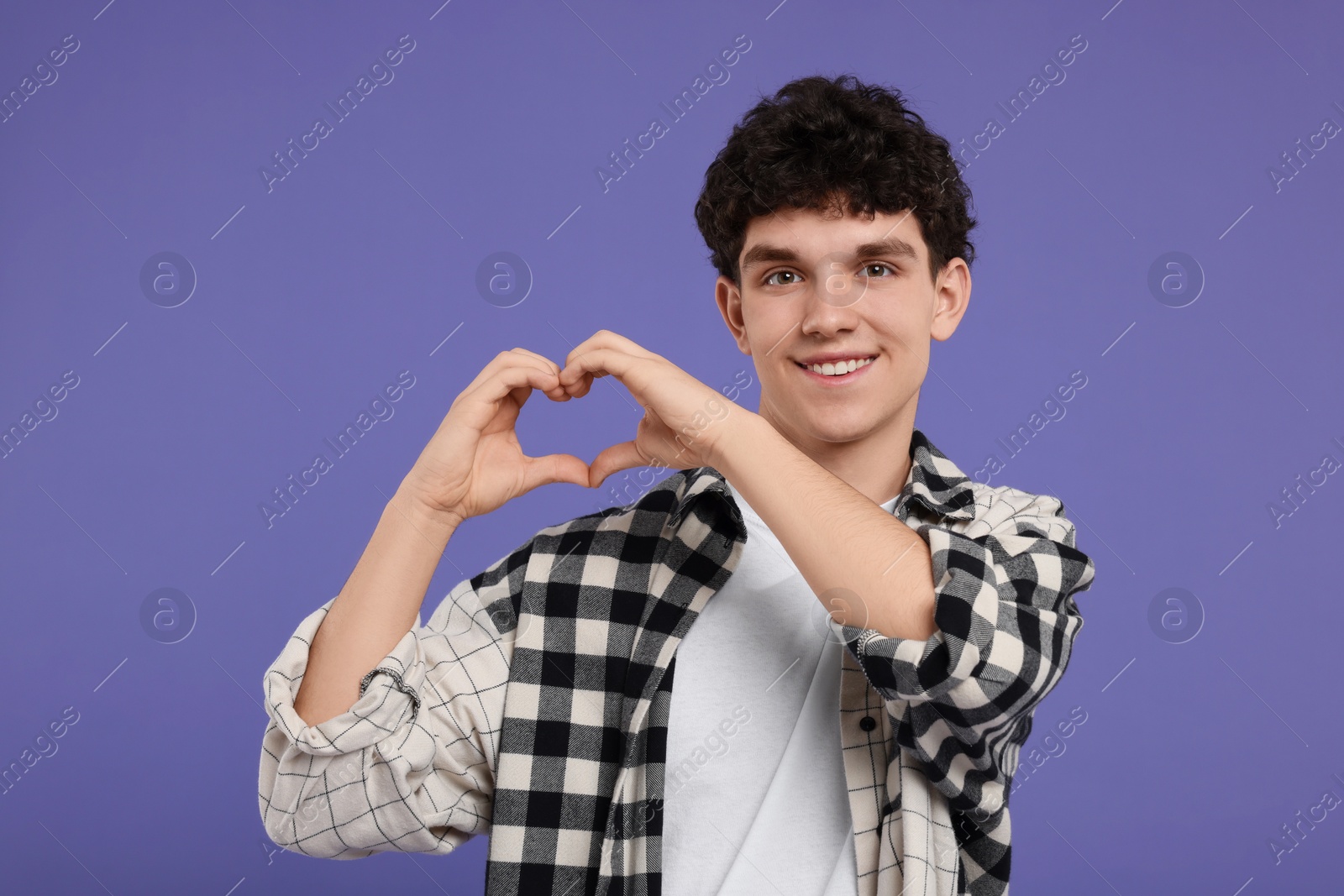 Photo of Happy young man showing heart gesture with hands on purple background