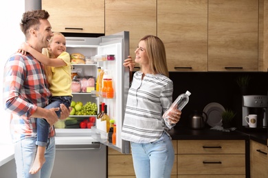 Photo of Happy family with bottle of water near refrigerator in kitchen
