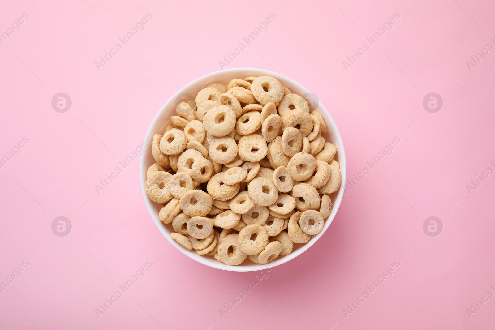 Photo of Tasty cereal rings in bowl on pink table, top view