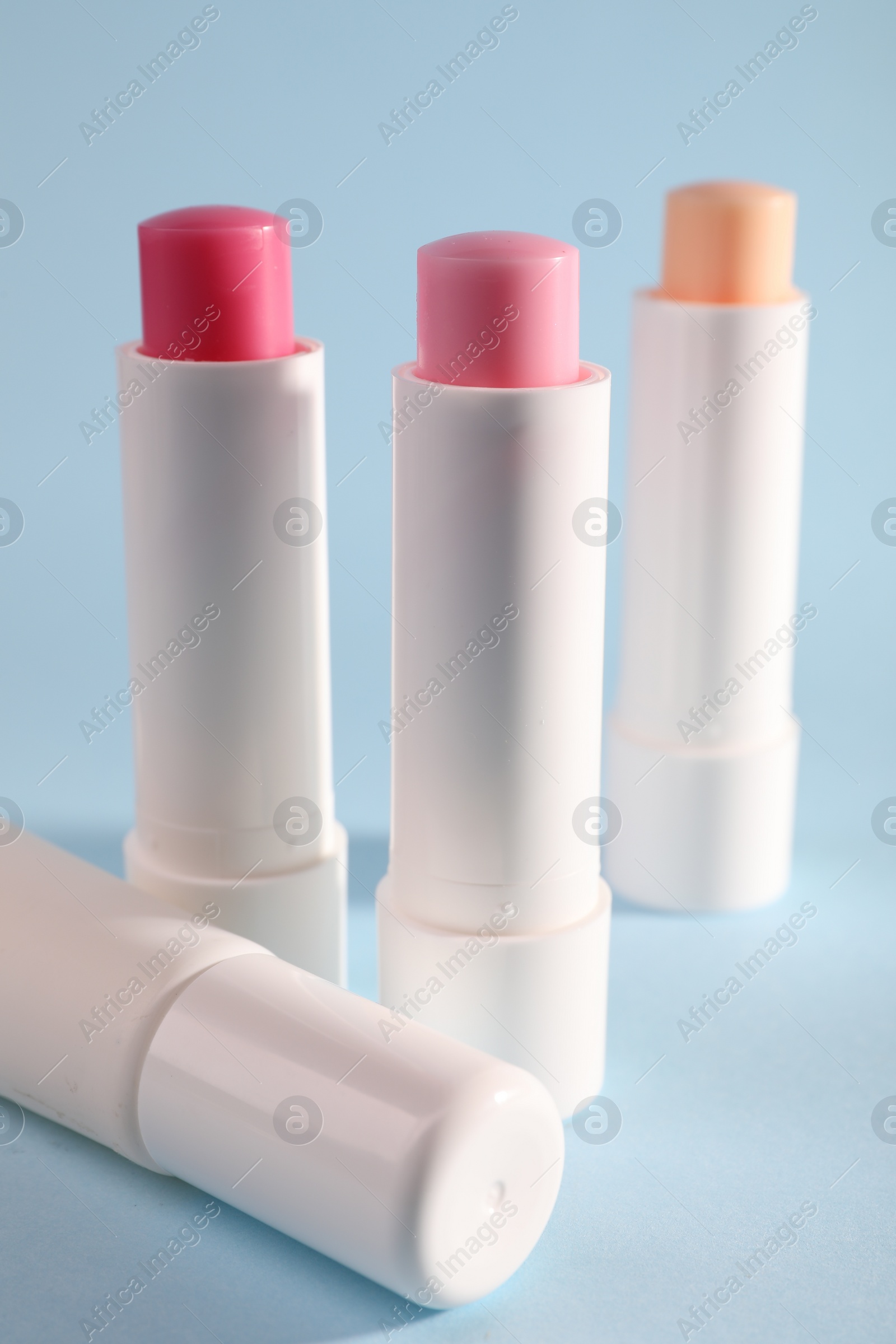 Photo of Different lip balms on light blue background, closeup