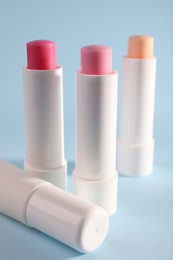 Photo of Different lip balms on light blue background, closeup