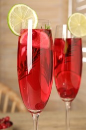 Tasty cranberry cocktail with rosemary and lime in glasses on table, closeup