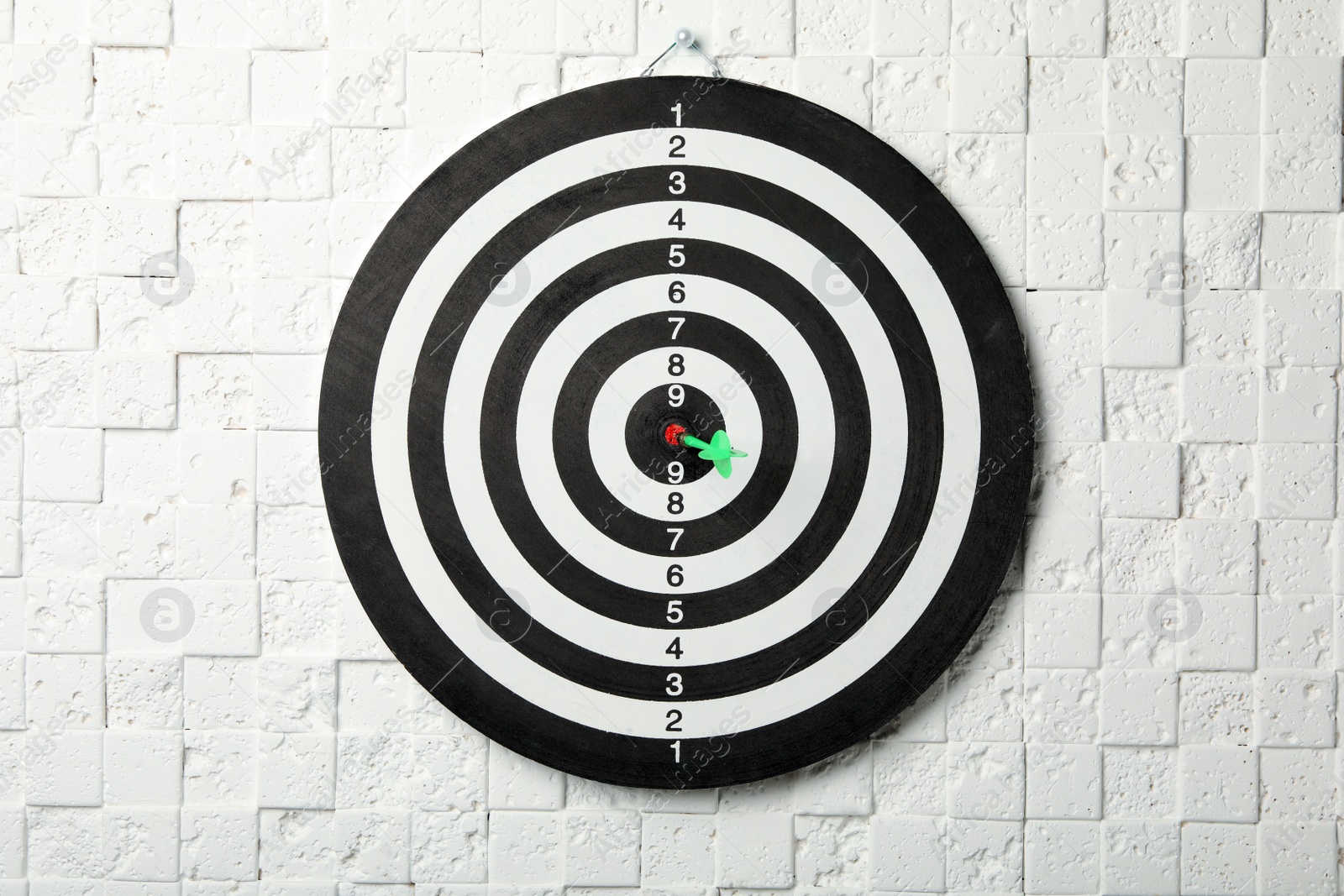 Photo of Dart board with arrow hitting target on white textured wall