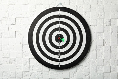 Photo of Dart board with arrow hitting target on white textured wall