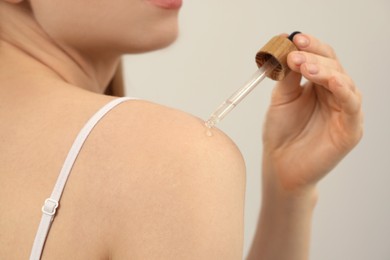 Woman applying essential oil onto shoulder on light background, closeup