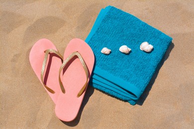 Folded soft blue beach towel with flip flops, seashells on sand, flat lay