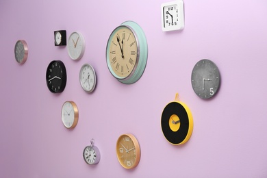 Photo of Many different clocks hanging on color wall. Time of day