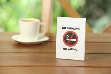 No Smoking No Vaping sign and cup of drink on wooden table outdoors. Space for text