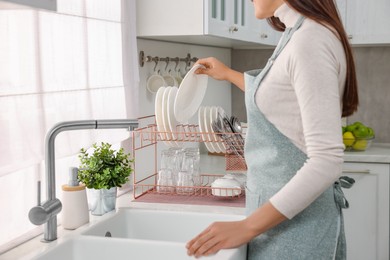 Woman putting clean plate on drying rack in kitchen, closeup