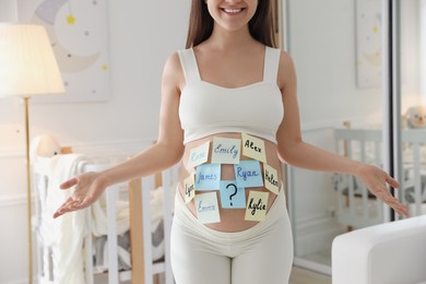 Photo of Pregnant woman with different baby names on belly at home, closeup