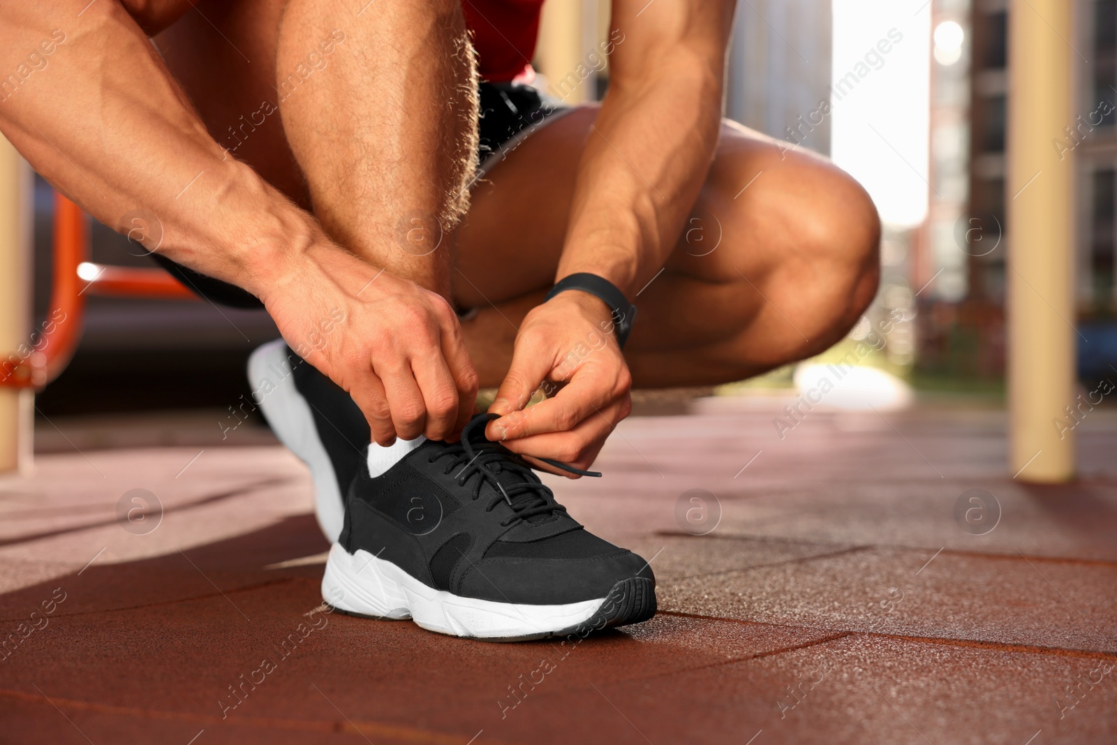 Photo of Man tying shoelaces before training at outdoor gym on sunny day, closeup