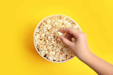 Photo of Woman taking fresh pop corn from bucket on yellow background, top view