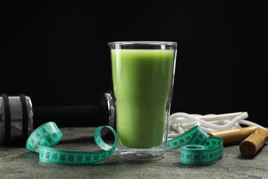 Photo of Tasty shake, sports equipment and measuring tape on grey table against black background. Weight loss
