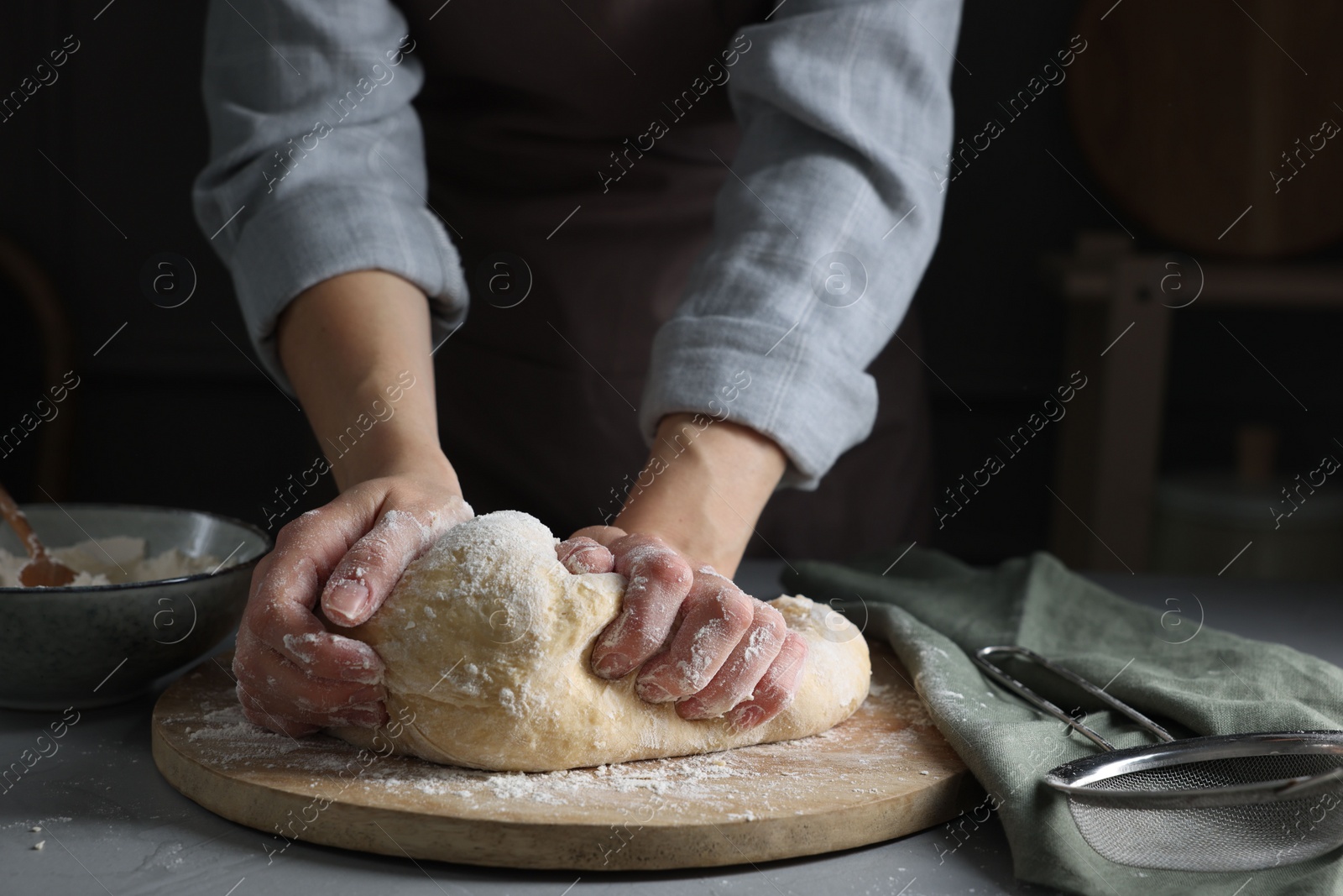 Photo of Woman kneading dough at grey table, closeup