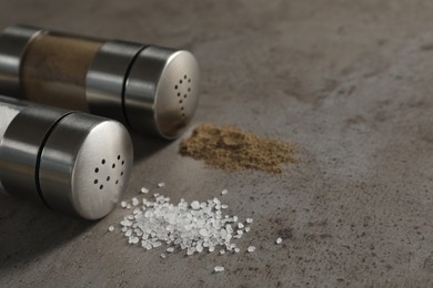 Photo of Salt and pepper shakers on grey textured table, closeup. Space for text