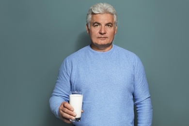 Mature man with dairy allergy holding glass of milk on color background