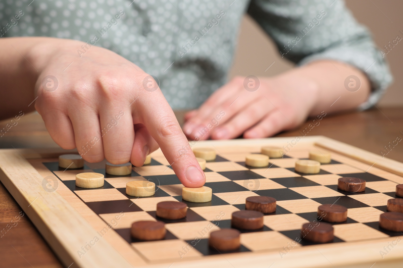 Photo of Playing checkers. Woman thinking about next move at wooden table, closeup