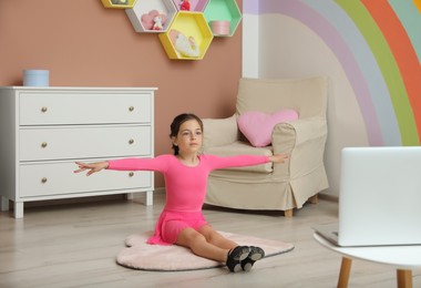 Photo of Cute little girl warming up before online dance class at home