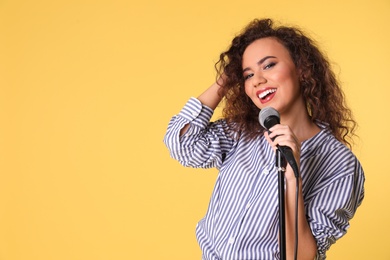 Photo of Portrait of curly African-American woman singing in microphone on color background. Space for text