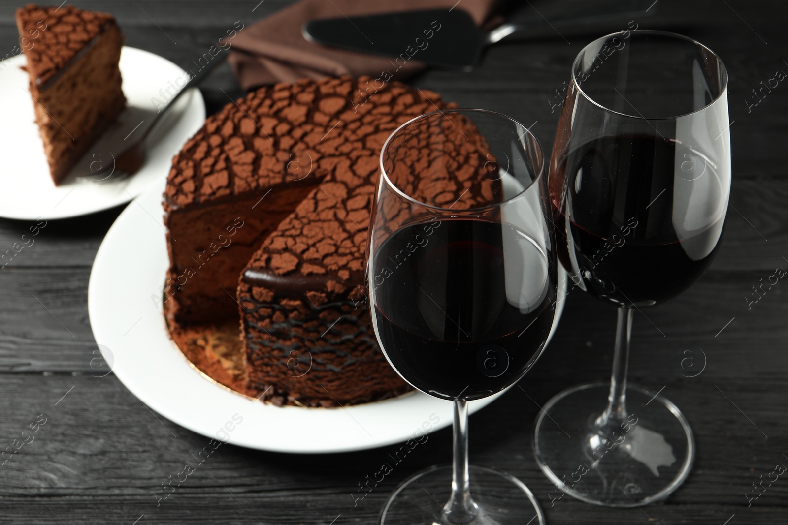 Photo of Delicious chocolate truffle cake and red wine on black wooden table