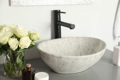 Photo of Vase with beautiful white roses and toiletries near sink in bathroom