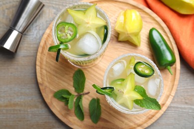 Photo of Glasses of spicy cocktail with jalapeno, carambola and mint on wooden table, flat lay