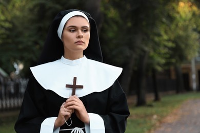Photo of Young nun with Christian cross in park outdoors, space for text