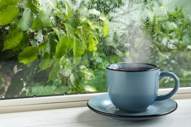 Image of Cup of hot drink near window on rainy day