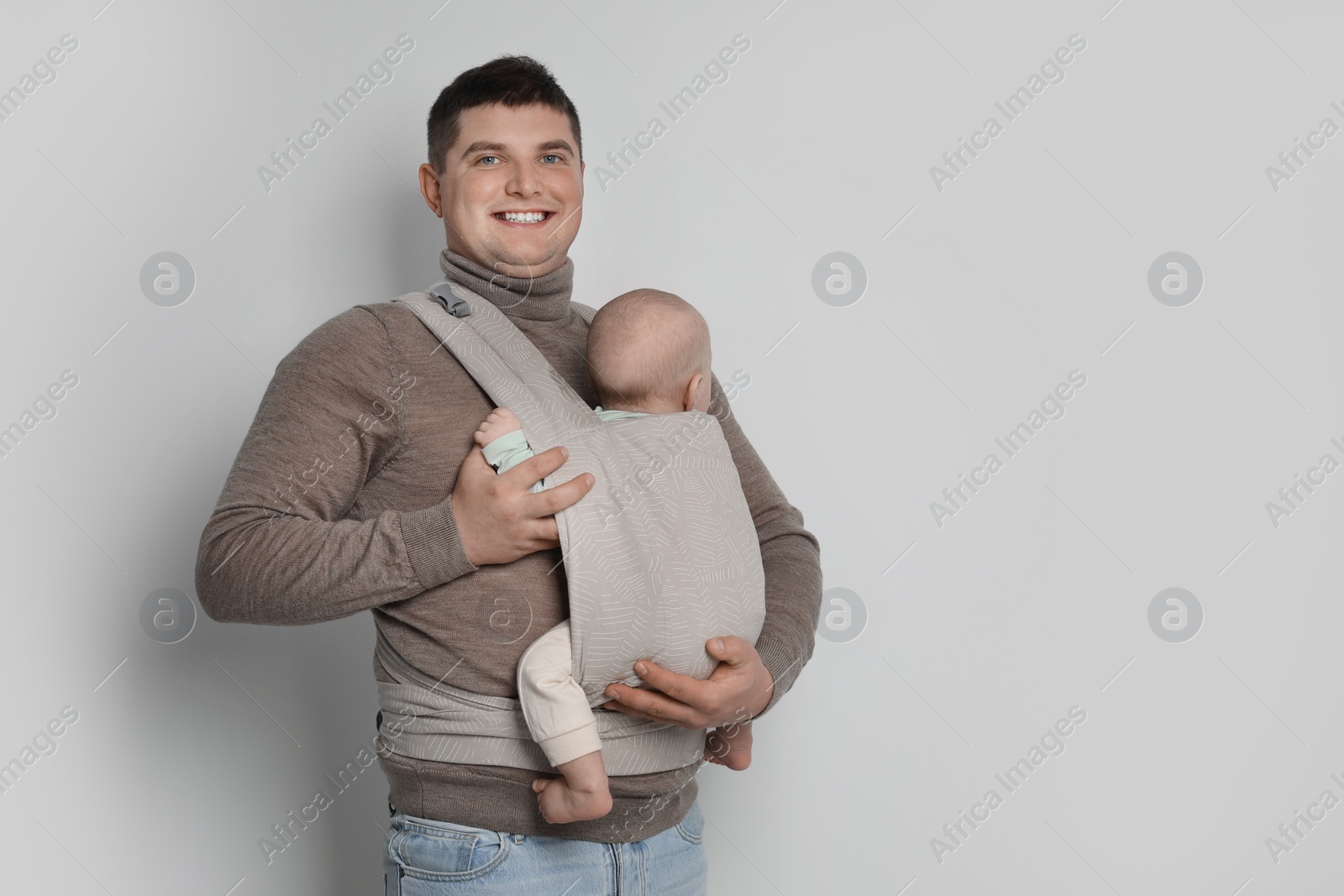 Photo of Father holding his child in sling (baby carrier) on light grey background. Space for text