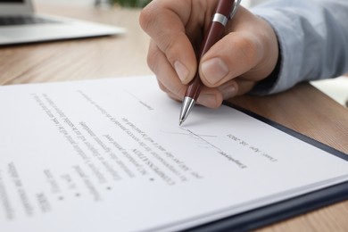 Photo of Man signing contract at wooden table, closeup